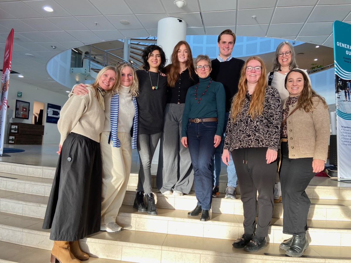 A group of ten smiling people stand together on indoor steps, in a well-lit space. They wear casual winter attire, conveying a joyful and friendly atmosphere.